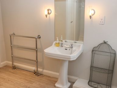 A bathroom with a pedestal sink mirror two wall lights a heated towel rail and a wire storage unit at Manor Cottage in Poulton