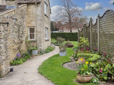 A garden path beside a stone house with flower pots and plants next to a wooden lattice fence at Manor Cottage in Poulton