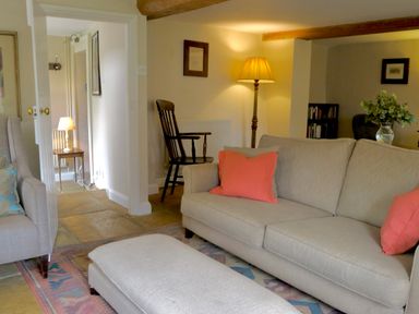 A living room with beige sofas and coral pillows a wooden chair a floor lamp and a small table with a lamp at Manor Cottage Poulton