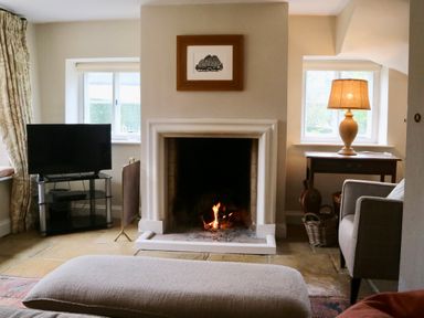 A living room with a fireplace fire a television on a stand and a table with a lamp at Manor Cottage in Poulton