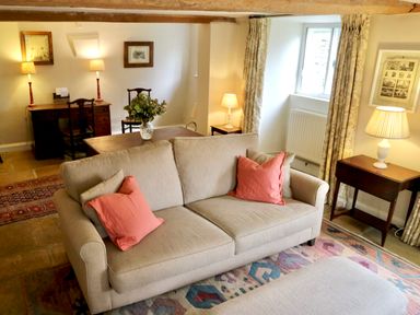 A beige sofa with red pillows in a living room with lamps and framed pictures at Manor Cottage in Poulton