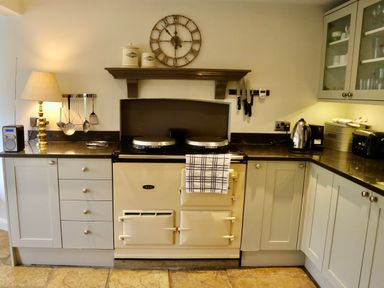 A kitchen with a stove oven a lamp on the countertop and kitchen utensils at Manor Cottage in Poulton