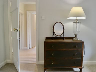 A wooden dresser with a round mirror and a table lamp next to an open door at Manor Cottage in Poulton