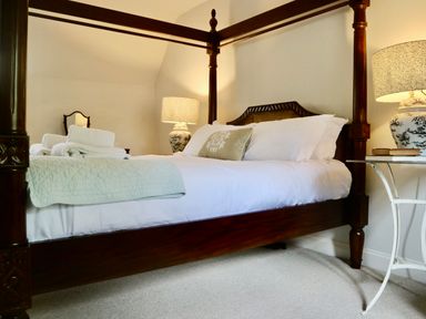 A bedroom with a four-poster bed white bedding bedside tables with lamps and folded towels at Manor Cottage in Poulton