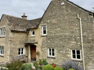 An exterior view of a stone house with wooden door white framed windows garden bench and plants in front at Manor Cottage in Poulton