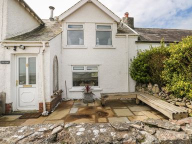 An outdoor patio area with stone paving a wooden bench and shrubs at 1 Salt Cottage in Port Eynon