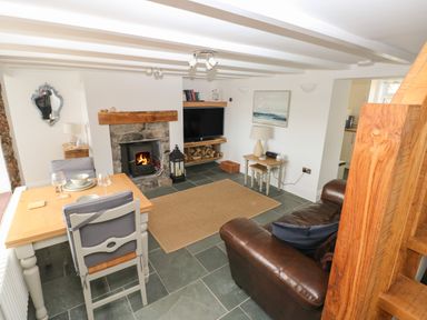 A living room with a fireplace a dining table a leather sofa and stairs at 1 Salt Cottage in Port Eynon