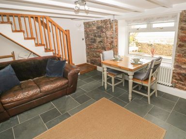 A living room with a brown leather sofa two chairs and a wooden table near a window at 1 Salt Cottage in Port Eynon