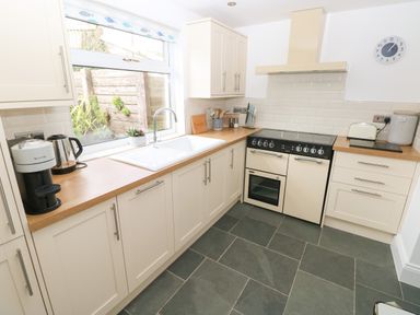 A kitchen with cream cabinets a wooden countertop a white sink a stove a kettle a coffee machine and a toaster at 1 Salt Cottage Port Eynon