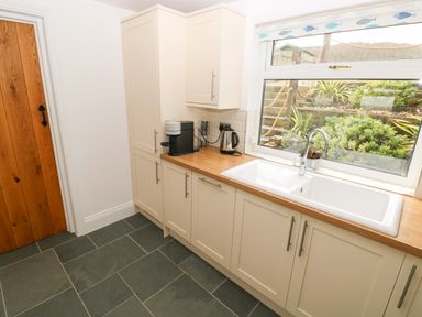 A kitchen with white cabinets a wooden countertop a coffee machine a kettle a large window with plants outside and a wooden door at 1 Salt Cottage in Port Eynon