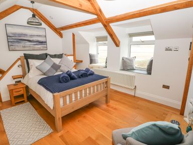 A bedroom with a wooden bed frame cushions on the bed and window seats at 1 Salt Cottage in Port Eynon