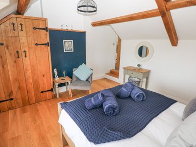 A bedroom with a bed covered with dark blue towels and blanket a wooden wardrobe a gray chair and wooden furniture at 1 Salt Cottage in Port Eynon