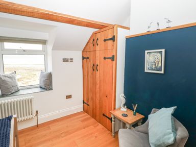 A corner of a room with a window seat with cushions a wooden storage cabinet a side table with decorations and a chair at 1 Salt Cottage in Port Eynon