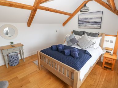 A bedroom with a wooden bed with blue and gray pillows and towels at 1 Salt Cottage in Port Eynon