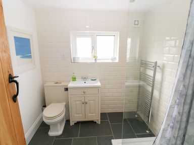 A bathroom with toilet sink cabinet window towel radiator and shower curtain at 1 Salt Cottage in Port Eynon