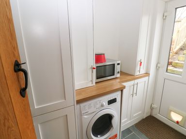 A utility room with a washing machine microwave and white cabinets at 1 Salt Cottage in Port Eynon