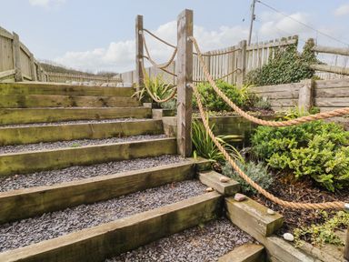 Outdoor wooden steps with rope railing and garden plants at 1 Salt Cottage in Port Eynon