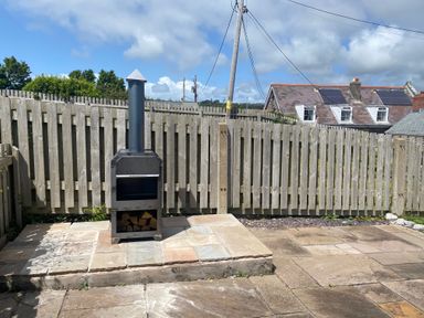 An outdoor patio with a metal wood-burning stove in front of a wooden fence at 1 Salt Cottage in Port Eynon