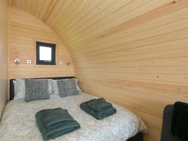 A bedroom with wood paneled curved walls a double bed with patterned bedding and folded towels on the bed at Green Fields in St Buryan