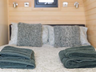 A bed with patterned bedding and two folded dark green towels with cushions on the headboard at Green Fields in St Buryan