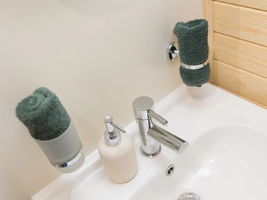 A bathroom sink with a chrome faucet soap dispenser and two rolled green towels at Green Fields in St Buryan