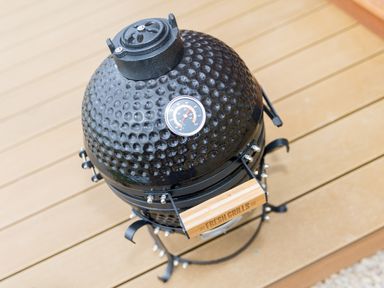 A black ceramic charcoal grill with a thermometer on the lid standing on a wooden deck at Green Fields in St Buryan