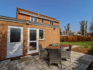 A brick house with two white doors and a small window overlooking a patio with a round table and four chairs at Robellen Corner in Adderbury