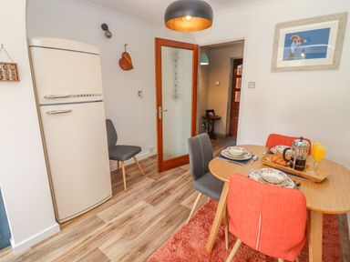 A dining area with wooden table set for breakfast with orange and gray chairs a cream refrigerator and a wooden door at Robellen Corner in Adderbury