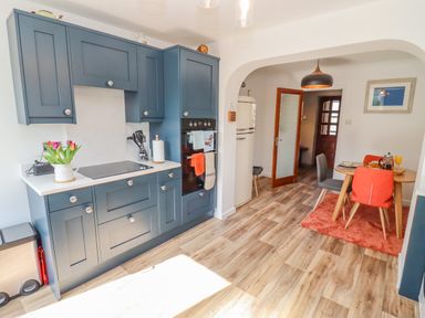 A kitchen with blue cabinets wood flooring and a small dining area with orange and gray chairs at Robellen Corner in Adderbury