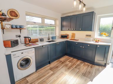 A kitchen with dark blue cabinets a washing machine toaster kettle and microwave at Robellen Corner in Adderbury