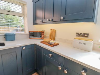A kitchen countertop with a microwave cutting boards bread and a bread box at Robellen Corner in Adderbury