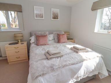 A bedroom with a double bed two bedside tables with lamps and two windows at Robellen Corner in Adderbury