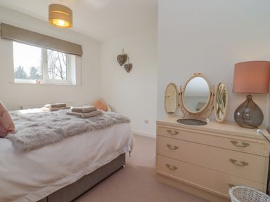 A bedroom with a bed covered in fur throws and towels beside a dresser with a trifold mirror and lamp at Robellen Corner in Adderbury