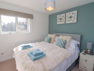 A bedroom with a bed with fluffy covers and blue towels on it a nightstand with a lamp and two flower paintings on the wall at Robellen Corner in Adderbury