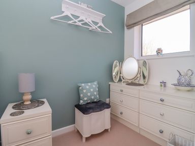 A dressing room with a white chest of drawers a cushioned stool and a window at Robellen Corner in Adderbury