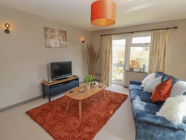 A living room with a blue sofa orange pillows a wooden coffee table a TV on a stand and a red rug at Robellen Corner in Adderbury