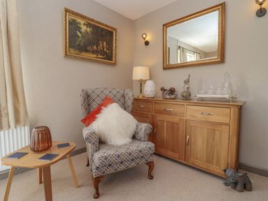 A sitting area with an armchair and two cushions next to a wooden sideboard with decorative items and a mirror at Robellen Corner in Adderbury
