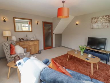 A living room with a blue sofa orange rug wooden coffee table and television at Robellen Corner in Adderbury
