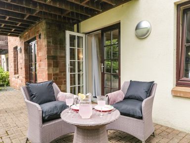 A patio with two cushioned chairs and a round table with a pitcher and glasses outside a building with open French doors at Cosy Corner in the Lakes in Greystoke