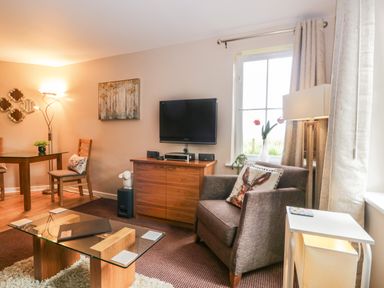 A living room with a glass coffee table a brown armchair and a wooden cabinet with a TV on it at Cosy Corner in the Lakes in Greystoke
