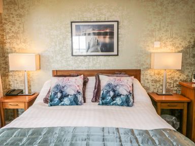 A bedroom with a double bed with decorative pillows two bedside tables with lamps and a framed picture above the bed at Cosy Corner in the Lakes in Greystoke