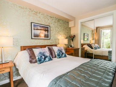 A bedroom with a bed pillows lamps bedside tables mirrored wardrobe and a window at Cosy Corner in the Lakes in Greystoke