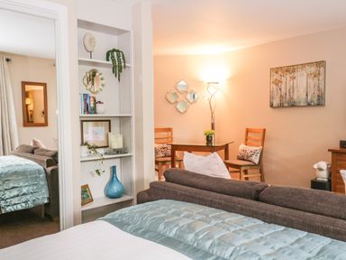 A bedroom with a bed and blankets next to a brown sofa and a dining table with chairs at Cosy Corner in the Lakes in Greystoke