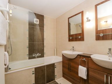 A bathroom with a bathtub a shower two sinks with mirrors and wooden cabinets at Cosy Corner in the Lakes in Greystoke