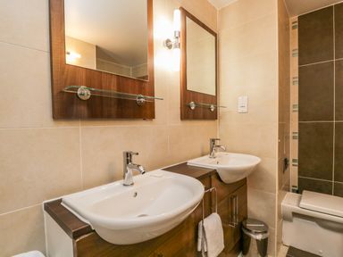 A bathroom with two sinks with mirrors above them and a toilet at Cosy Corner in the Lakes in Greystoke