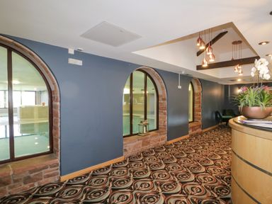 A hallway with arched windows looking into a pool area a curved reception desk and patterned carpet at Cosy Corner in the Lakes in Greystoke