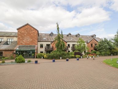 The exterior view of a multi-story brick and stone building with balconies and a green entrance canopy labeled Whitbarrow at Cosy Corner in the Lakes Greystoke