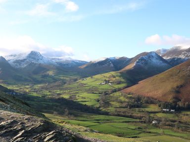 A valley with green fields and scattered houses surrounded by snow capped mountains at Cosy Corner in the Lakes in Greystoke