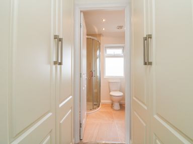 A bathroom with a shower and toilet viewed from a hallway with white closet doors at Ridges Retreat No 7 Kigbeare Lodges Ashbury Resort near Fowley Cross Sourton Down and Okehampton