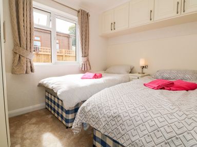 A bedroom with two single beds with patterned bedding and pink towels near a window at Ridges Retreat No 7 Kigbeare Lodges Ashbury Resort near Fowley Cross Sourton Down and Okehampton